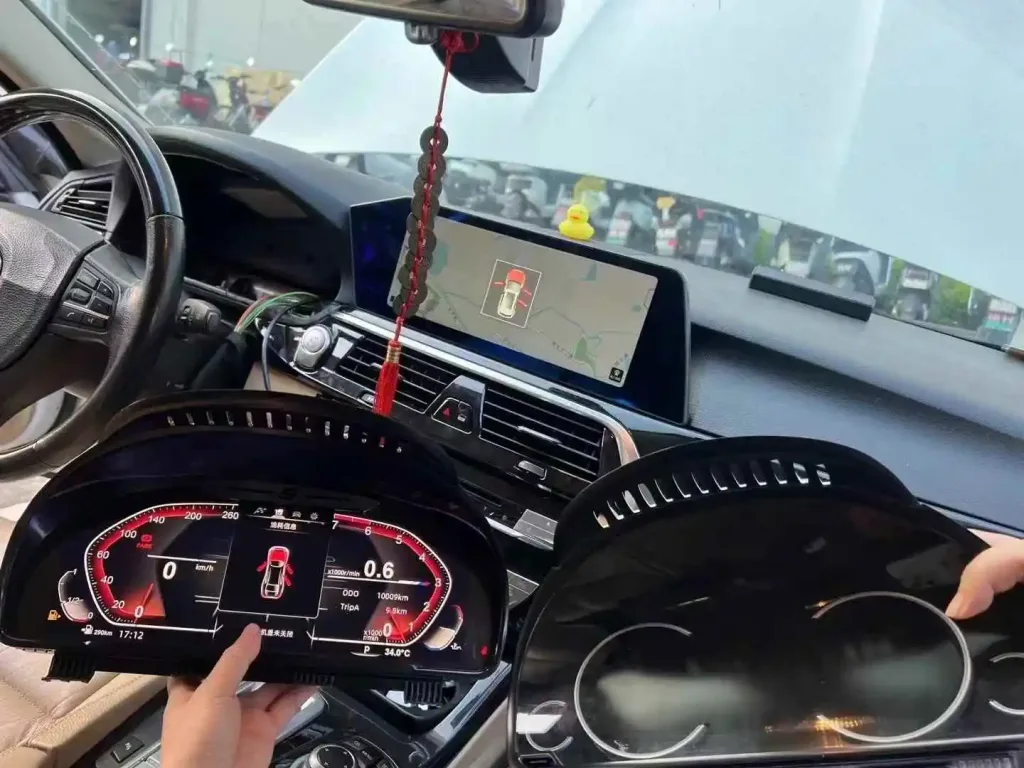 BMW digital cluster compared with original instrument cluster inside vehicle during installation